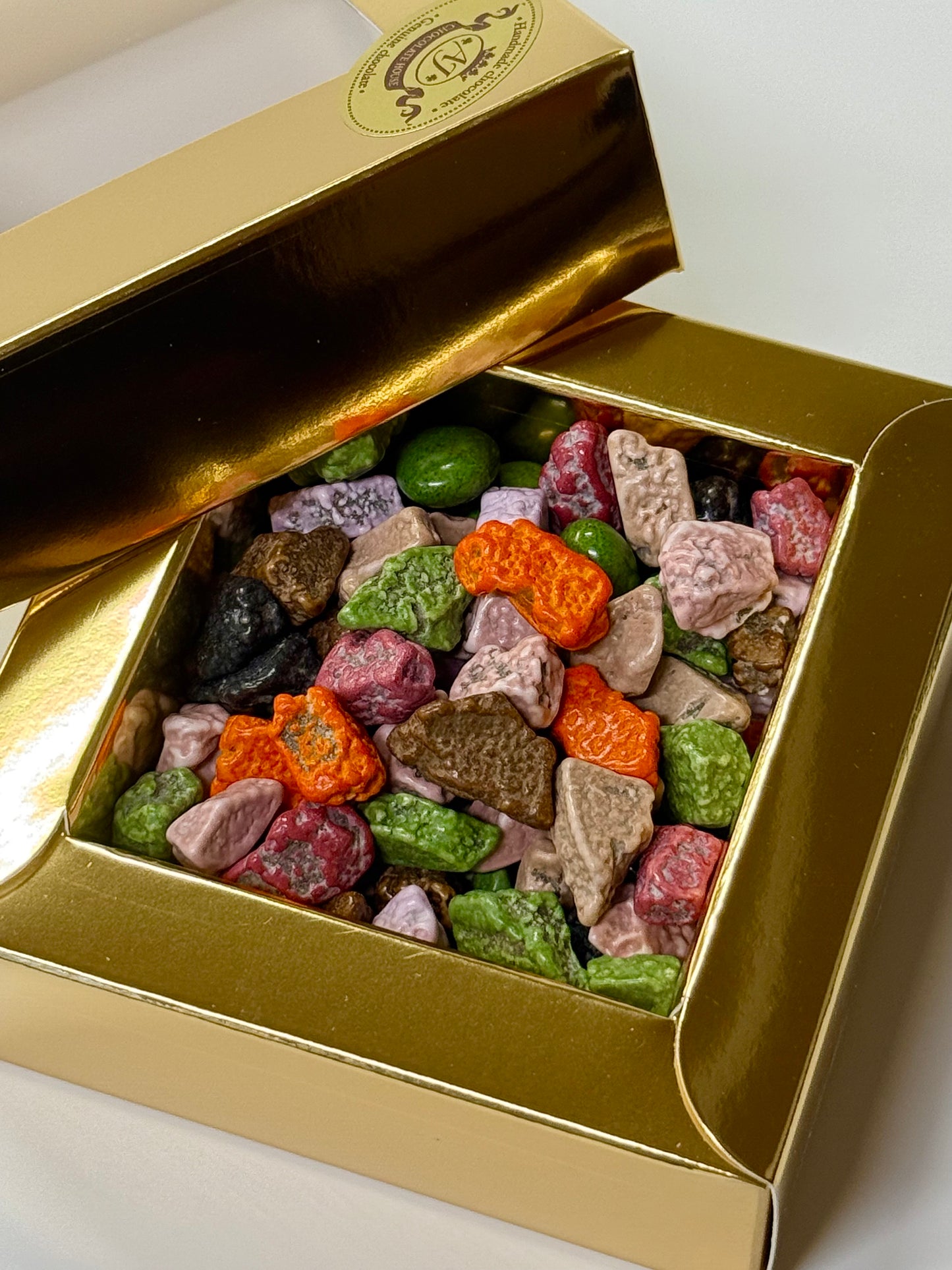 Dražė spalvoti šokoladiniai akmenėliai auksinėje dėžutėje, 100 gr.